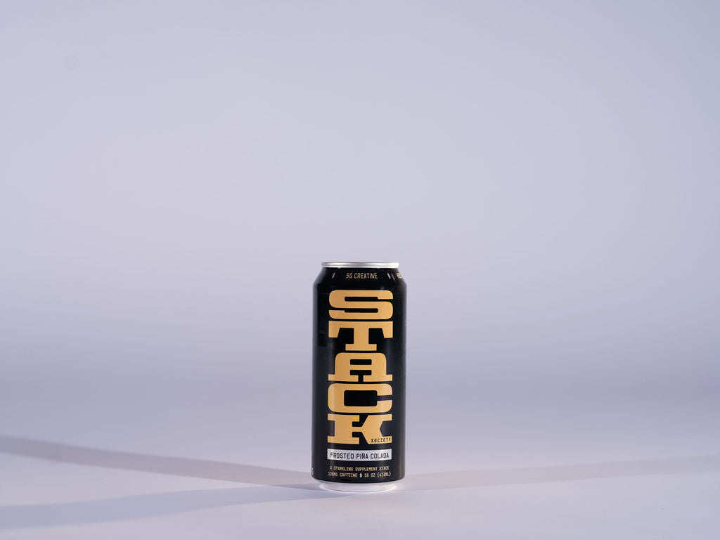 A single black aluminum can of STACK Supplement Drink with bold yellow lettering, standing upright on a light gray surface against a matching light gray background.