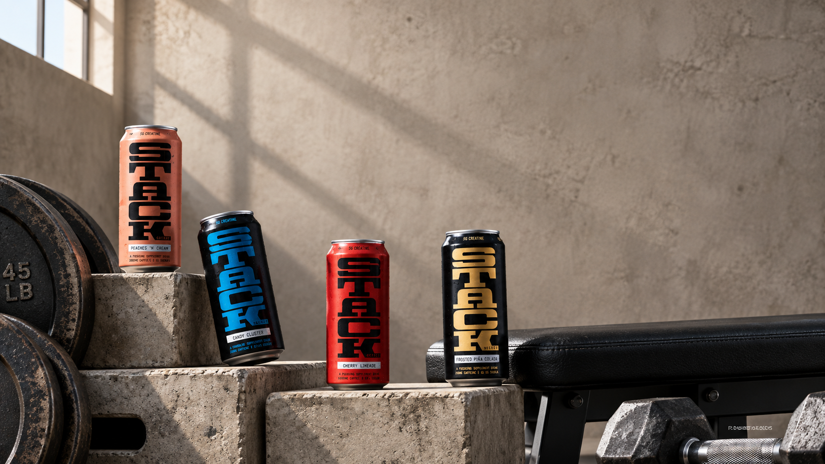 Four STACK Society flavor cans arranged with gym weights and a bench